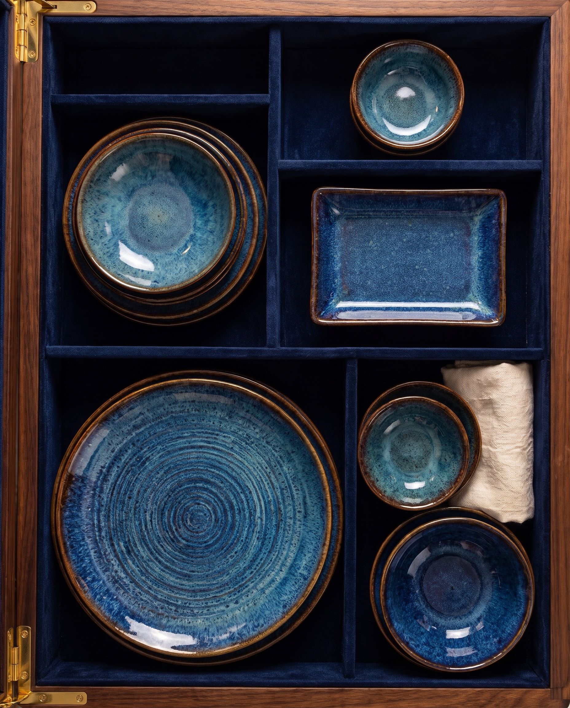 Blue-glazed NEELĀ plates, bowls and a rectangular dish from above, each in its own navy velvet place in the walnut chest